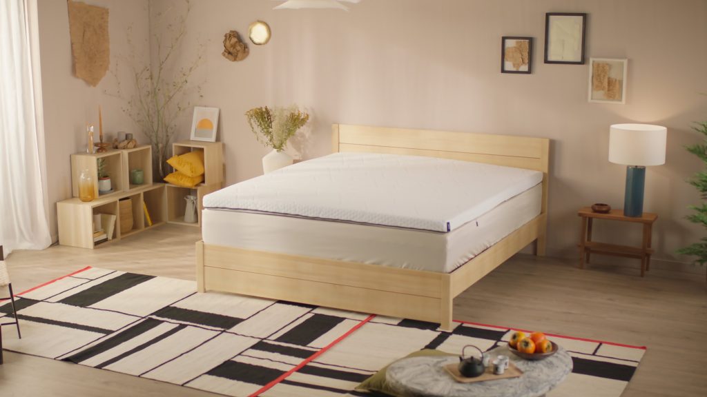 Sobrecolchão Emma Original Pro sobre uma cama de madeira num quarto com tapete