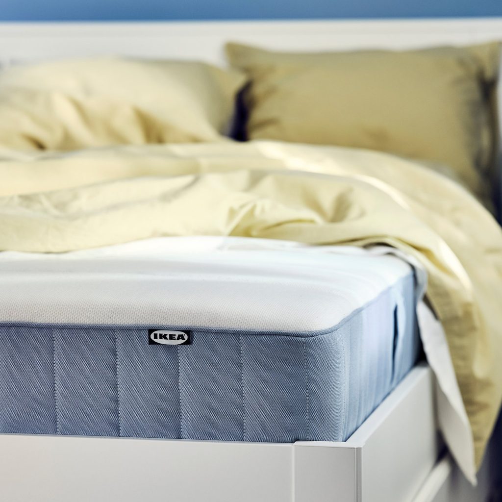 IKEA VESTERÖY, canto do colchão sobre uma cama branca com roupa de cama amarela