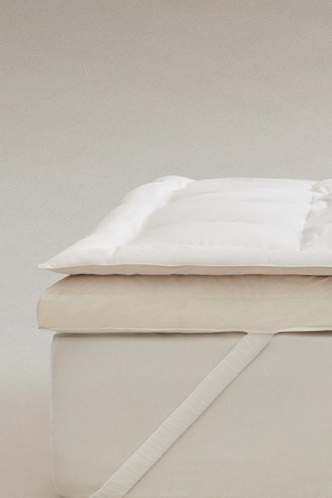 Topper de Colchão com Penugem da Zara Home sobre um colchão bege, com a fita elástica no canto